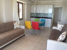 Una sala de estar con sofá y sillones, una mesa de comedor y una cocina con armarios y salpicadero de azulejos.