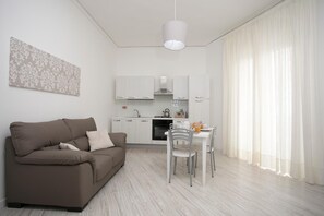 Una sala de estar moderna con un sofá marrón, una mesa de comedor con sillas y una zona de cocina al fondo.