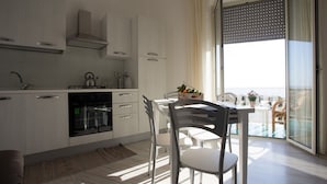 A modern kitchen with white cabinetry, a built-in oven, and a dining area with a table and chairs. - Aria Di Mare B&b (Marsala)