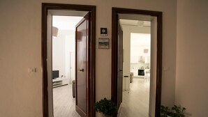 A hallway with a wooden door leading to a living area with a TV and a sofa. There is a potted plant in the hallway. - Aria Di Mare B&b (Marsala)