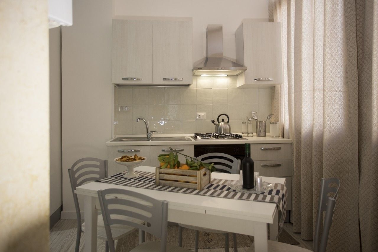 A compact kitchen with white cabinets, a gas stove, and a dining area with a checkered tablecloth.