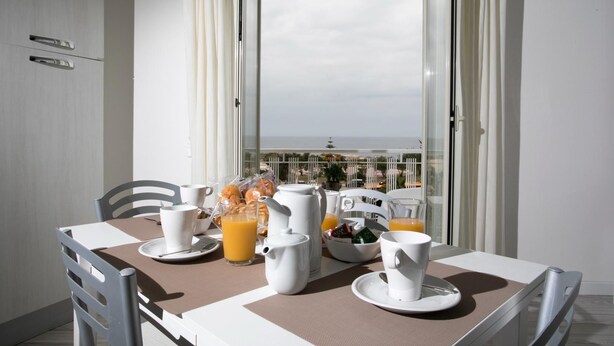 A breakfast table with white tableware, a pitcher, and orange juice, set against a balcony with a view of the sea. - Aria Di Mare B&b (Marsala)