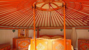 Eine traditionelle Jurte mit einem Himmelbett, aufwendigen Holzmöbeln und einem Spiegel.
