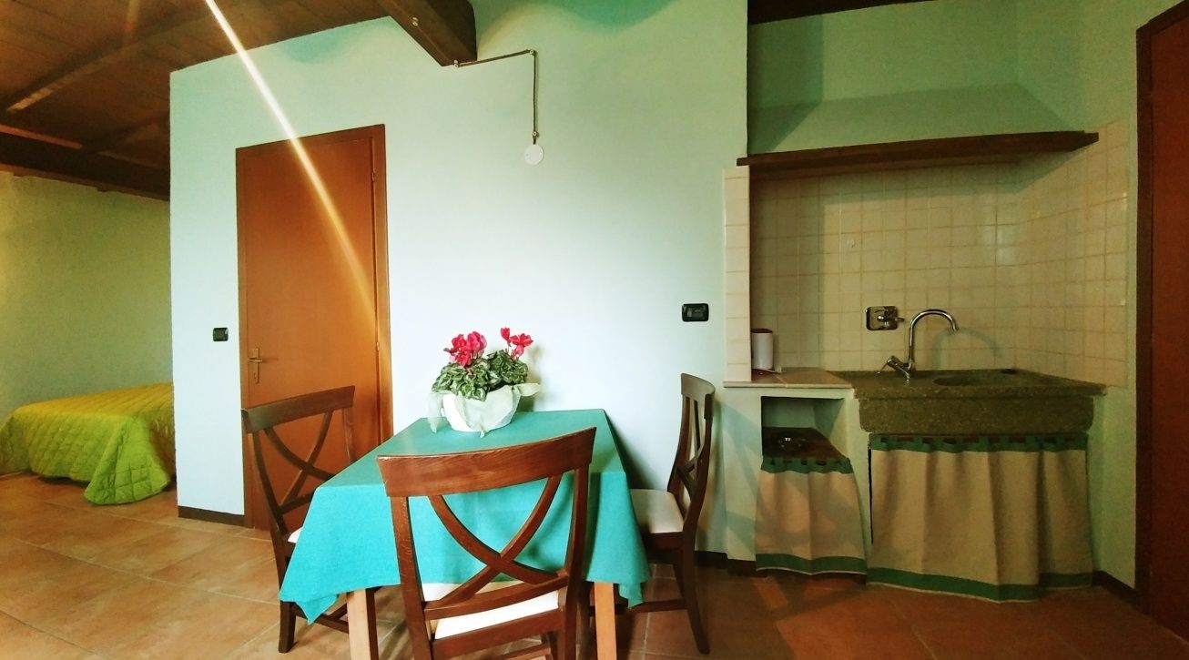 A small, cozy room with a dining table and chairs, a kitchen area with a sink and countertop, and a door leading to another room.