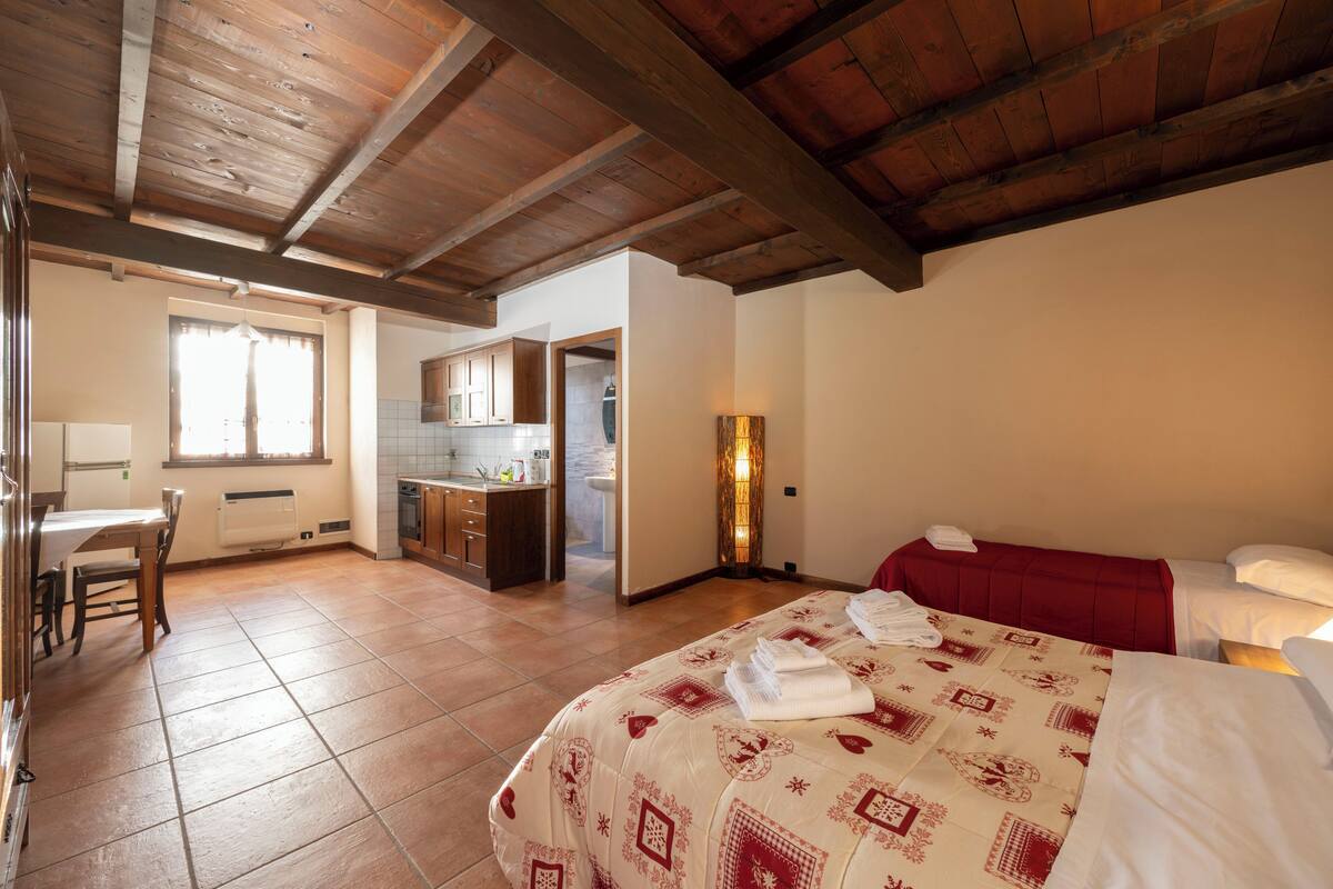 A bedroom with a bed, a desk, and a kitchenette.