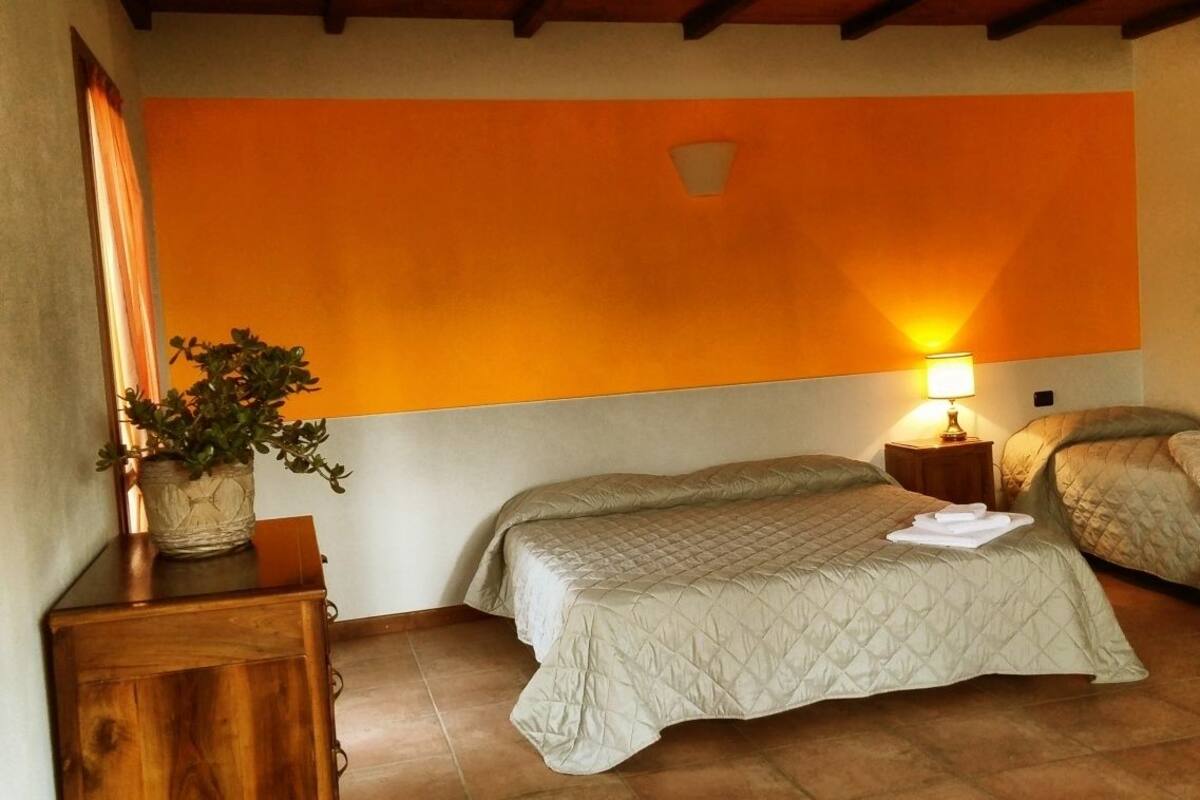 A room with two beds, a nightstand with a lamp, a potted plant, and a wooden cabinet.