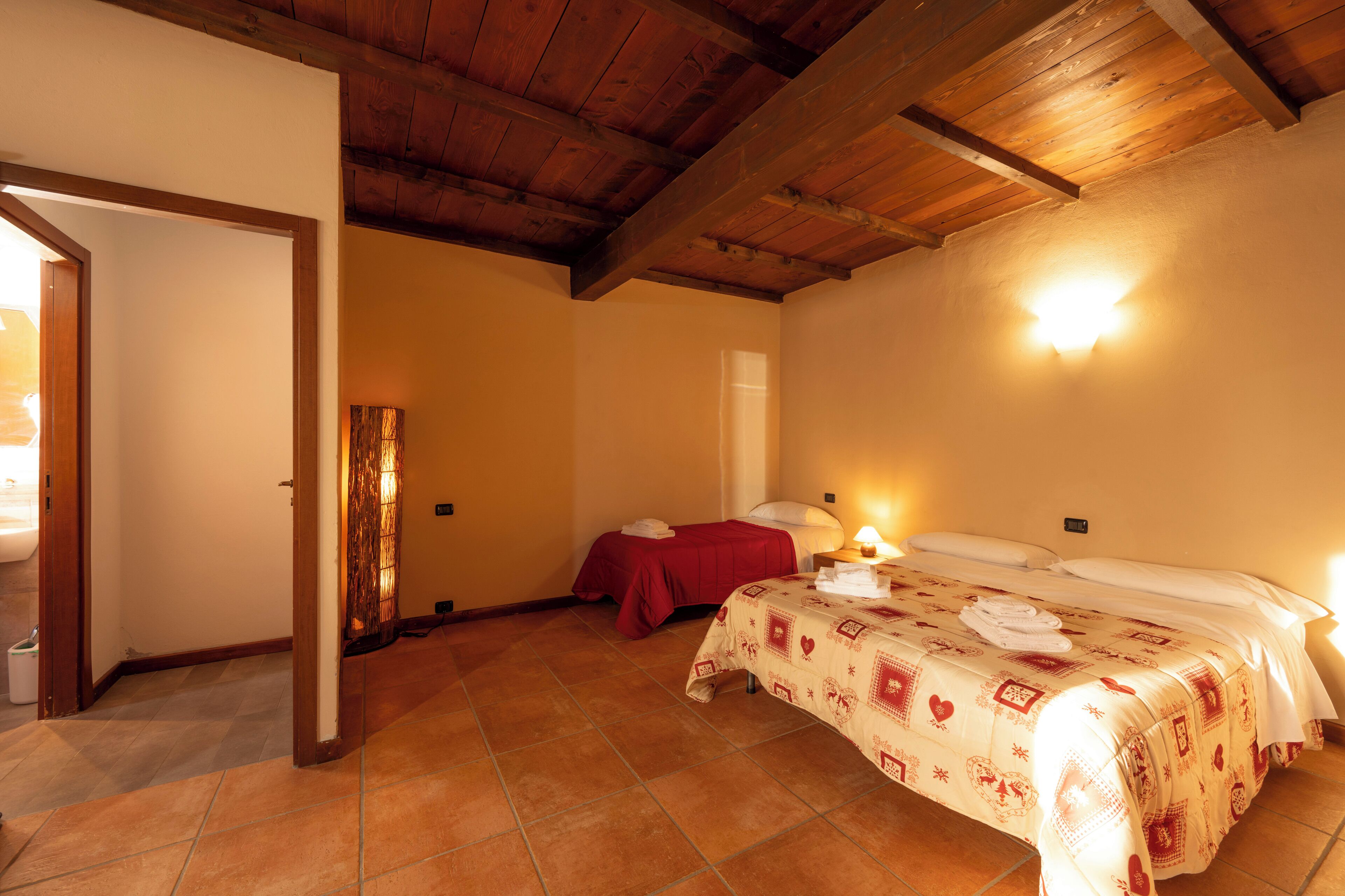 A room with two beds, a wooden ceiling, and a tiled floor.