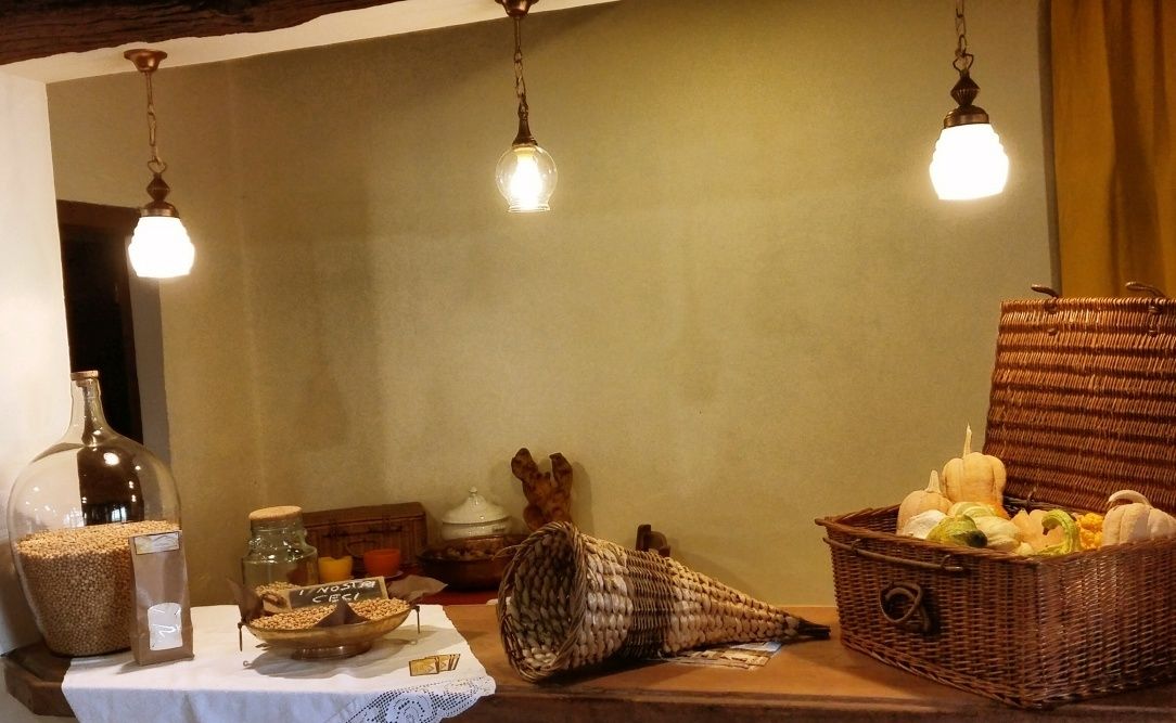 A rustic interior with a wooden table displaying various items like a glass jar, a woven basket, and a wicker basket filled with pumpkins.