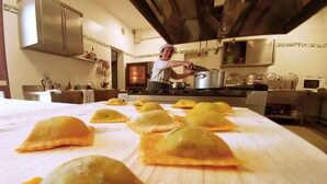 A kitchen with a table covered in ravioli, a stove, and a person cooking. - Agriturismo di Sordiglio (Casina)