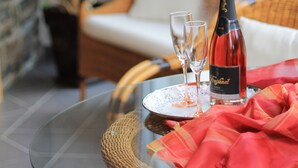 A glass table with a bottle of champagne, two glasses, and a red napkin on a wicker chair in a room with a stone wall and a white sofa. - Pension & Ferienwohnung Schweinsberg (Medebach)
