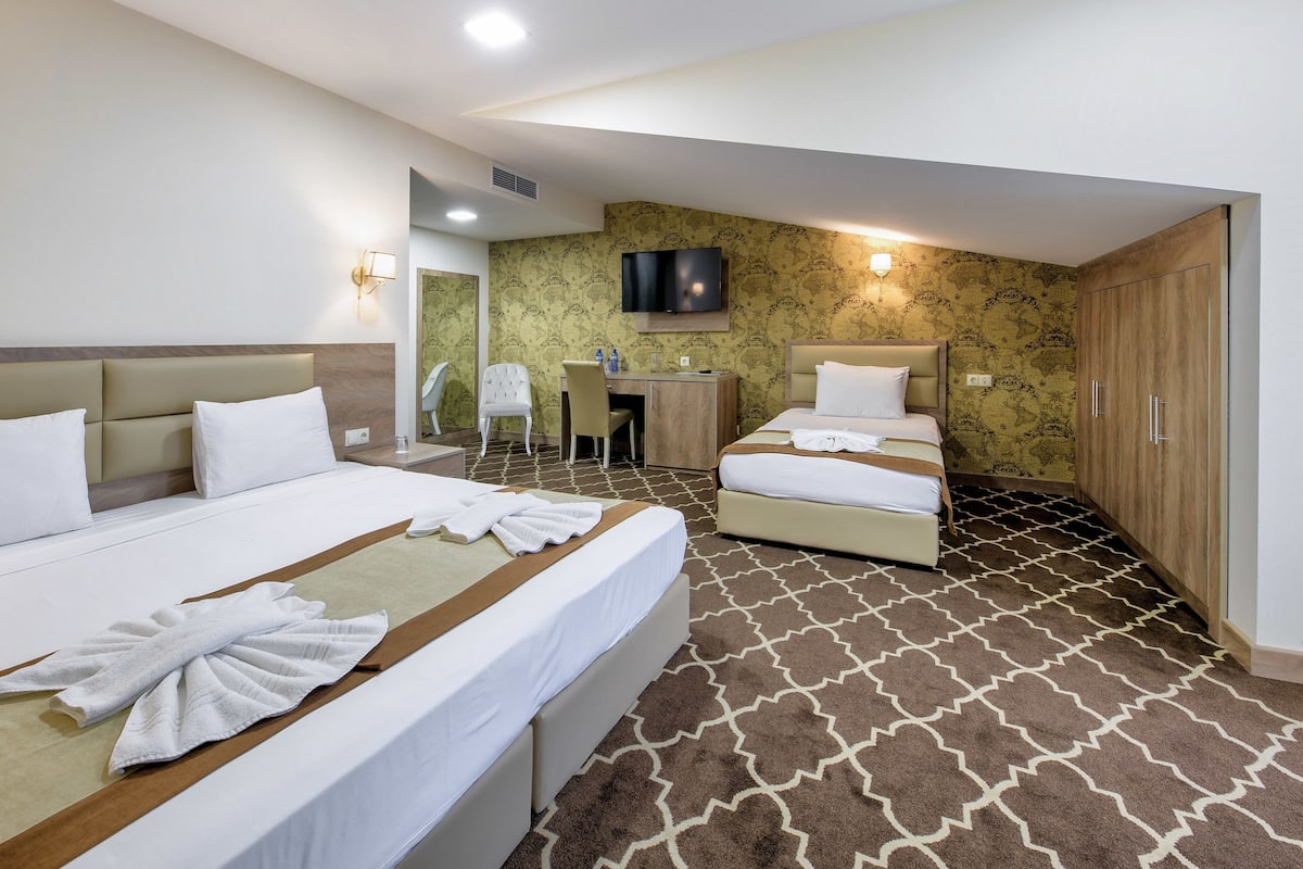 A hotel room with two beds, a desk, a chair, a TV, and a wardrobe.