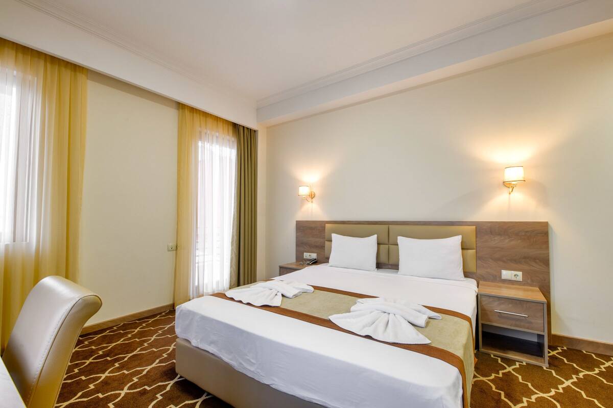 A hotel room with a large bed, two bedside tables, a chair, and a window with curtains.