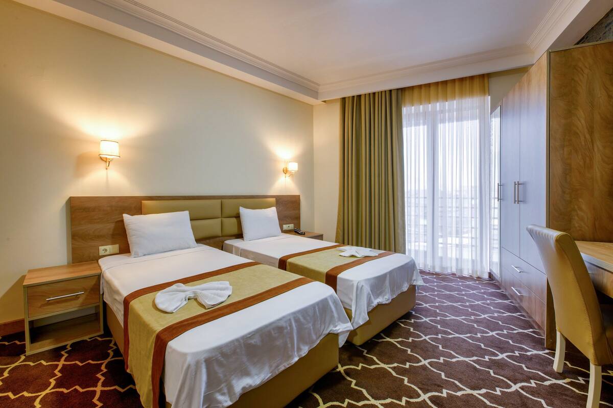 A hotel room with two beds, a desk, a chair, a nightstand, and a window with curtains.