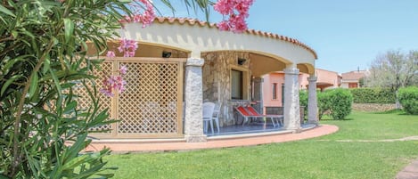 Un área de estar al aire libre cubierta, con un muro de piedra, una silla blanca y una mesa.