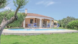 A house with a swimming pool, lounge chairs, and a stone wall surrounding the pool.