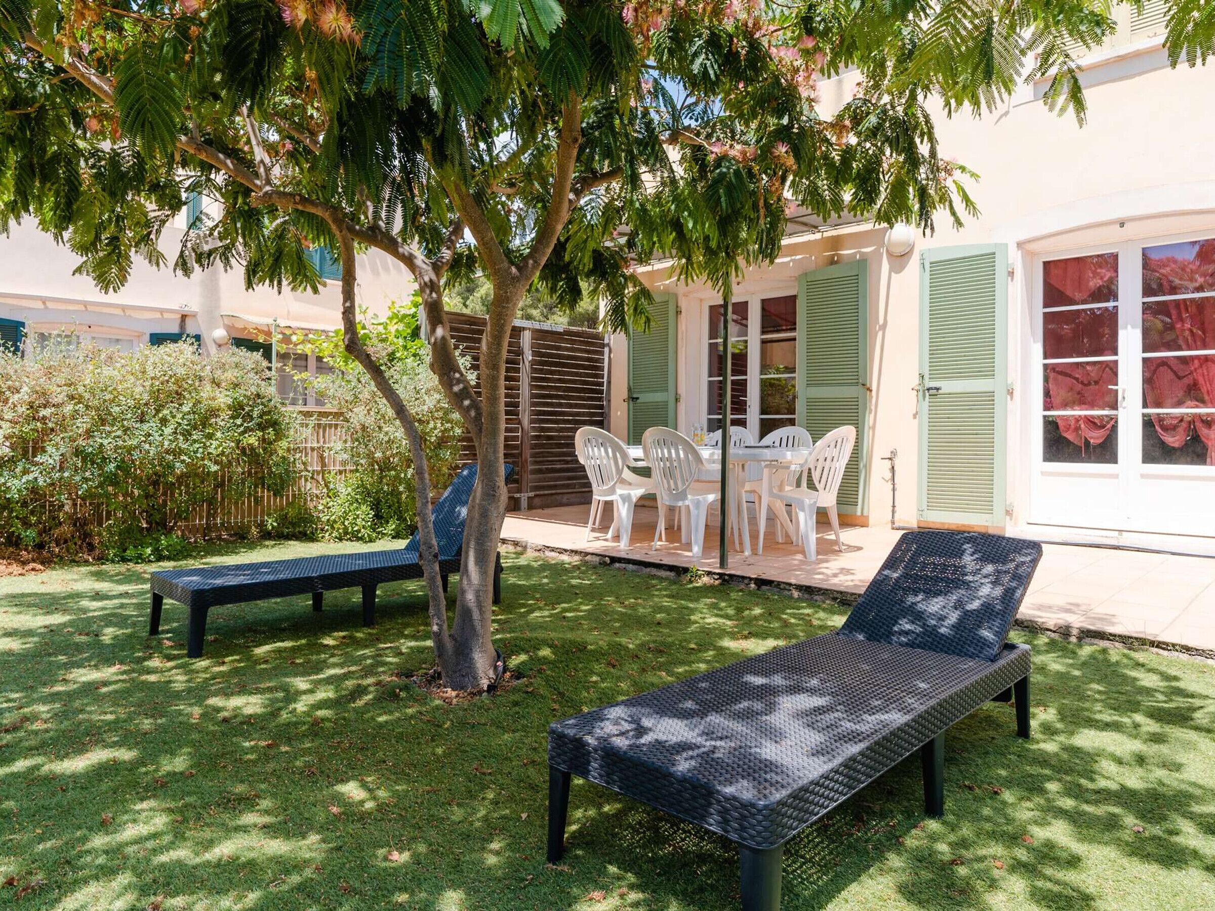 Un patio con dos sillones, una mesa con sillas y una zona de estar cubierta con vista a la casa.