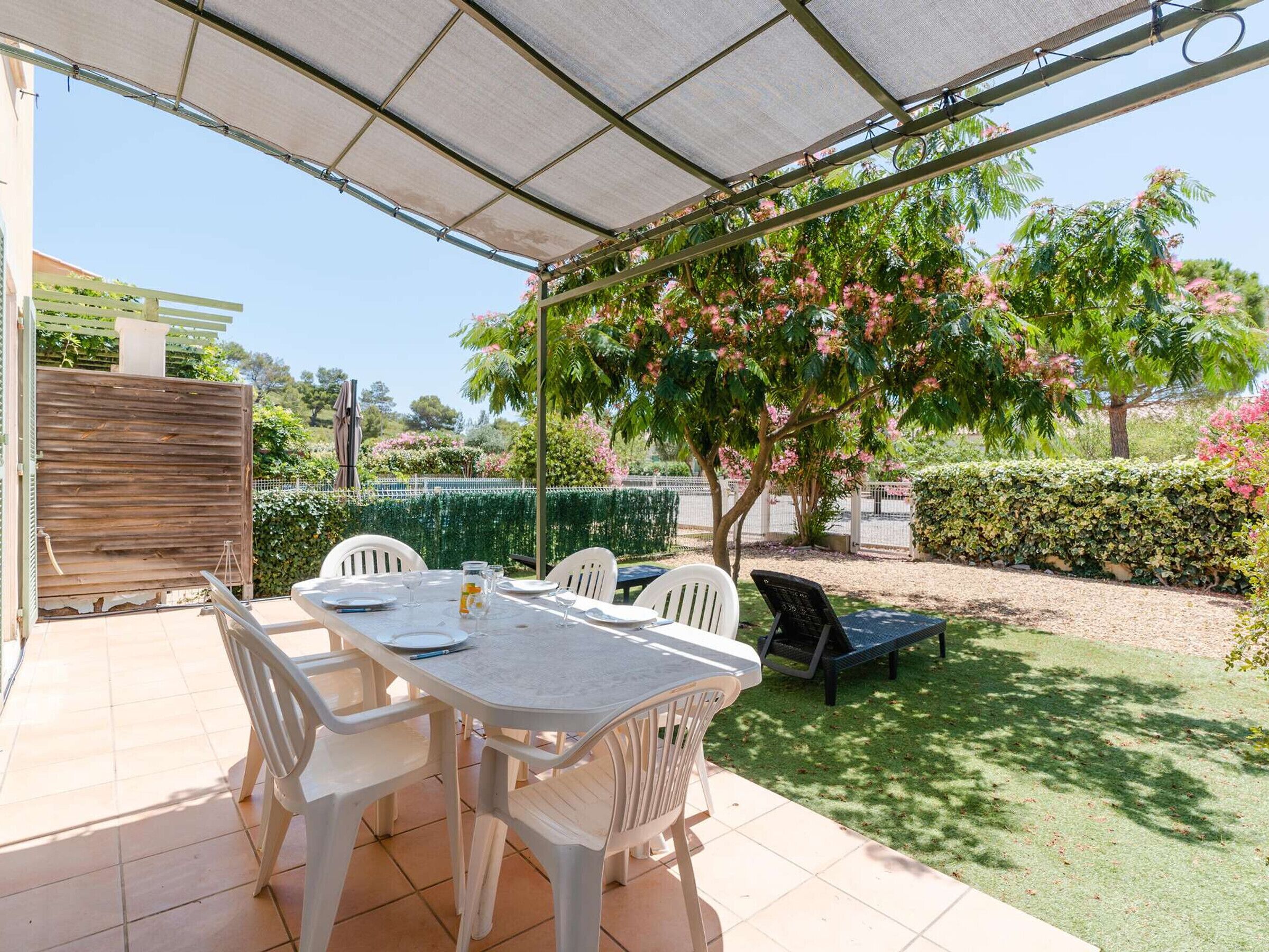 An outdoor patio with a table and chairs, a grill, and a pergola providing shade.