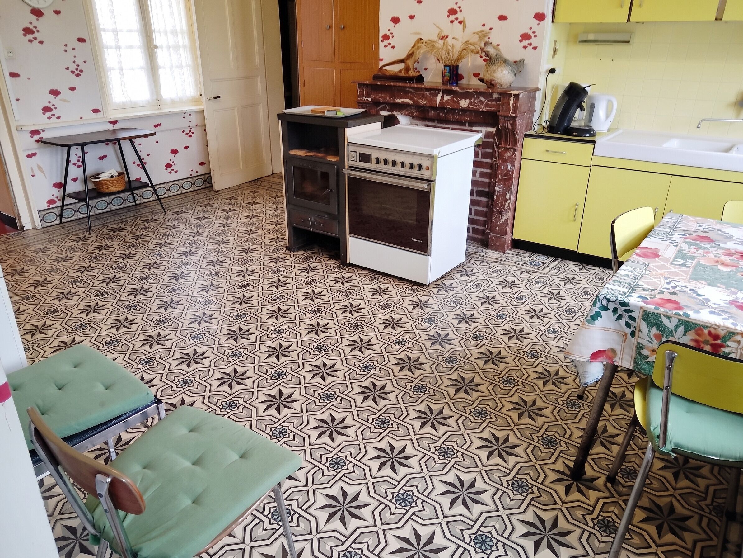 A kitchen with patterned floor tiles, a stove, a sink, and yellow cabinets.