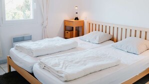 A double bed with white bedding and two pillows, a bedside table with a lamp, and a window with curtains. - Charming 4-Room Villa with Terrace & Garage - Sleeps 5, Narbonne-Plage (Narbonne-Narbonne Plage-Narbonne Plage)