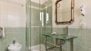 A bathroom with a glass shower enclosure, a glass sink, a bidet, and a mirror with a hairdryer on the wall. - Domus Bella Roma (Rome)