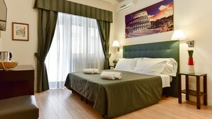 A hotel room with a bed, a desk, a chair, a lamp, and a painting of the Colosseum. - Domus Bella Roma (Rome)