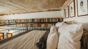 A room with a large bed, a bookshelf filled with books, and framed pictures on the wall.