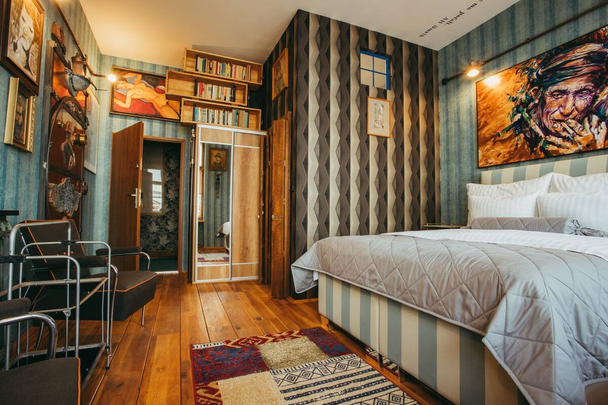 A bedroom with a bed, a chair, a bookshelf, and a door leading to another room.