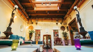 A library with wooden bookshelves, a central reading area with chairs, and a chandelier.