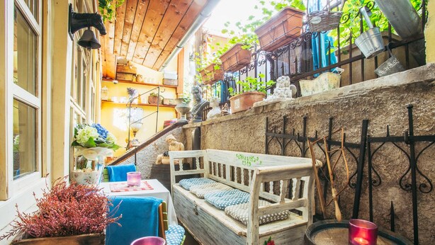 A cozy outdoor seating area with a wooden bench, a table with a candle, and various potted plants.