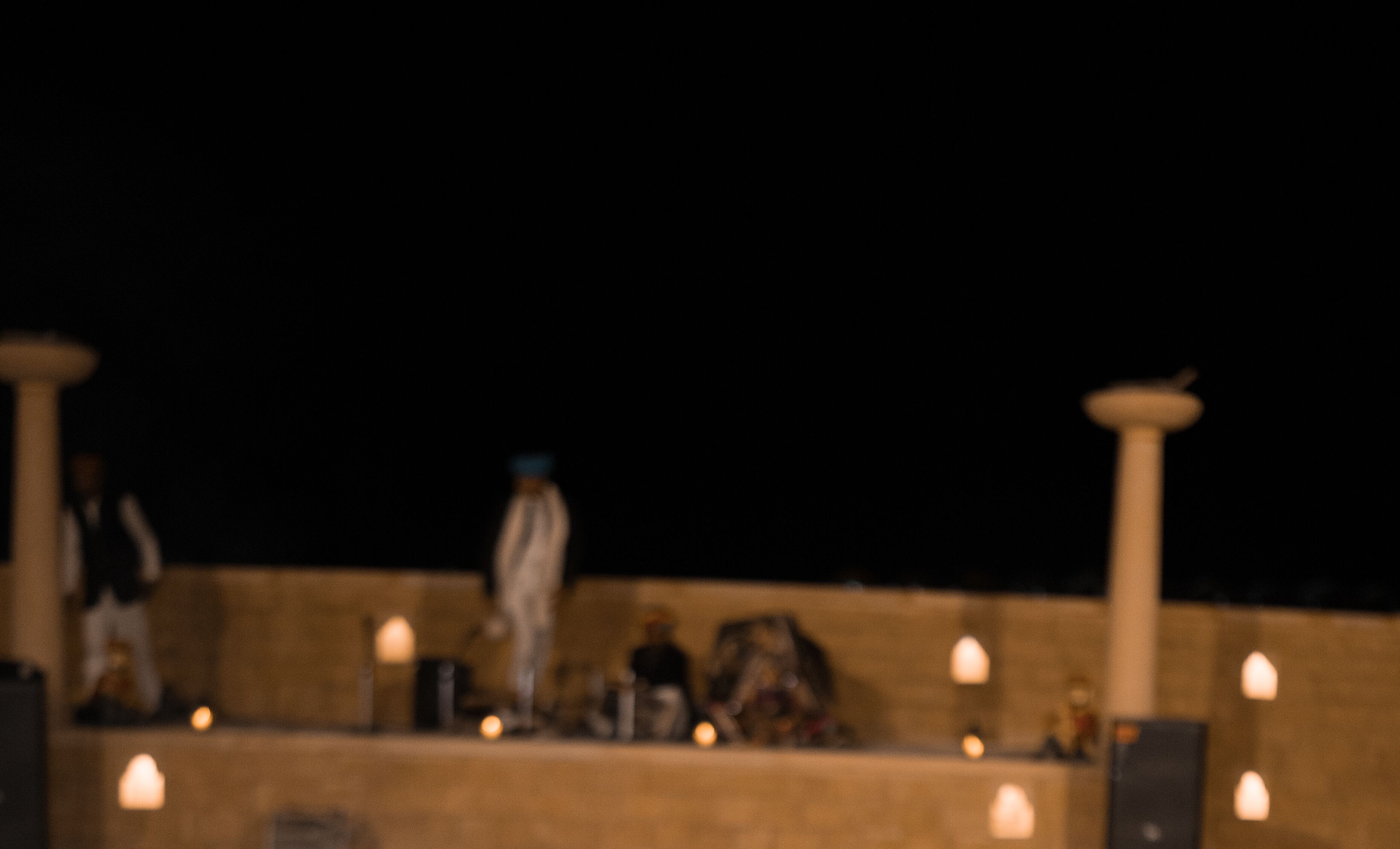 A dimly lit outdoor area with a stone wall and several people standing.