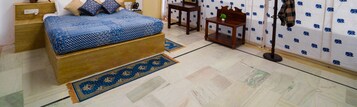 Un dormitorio con cama, una mesita de noche, una pequeña noche y una lámpara de pie, además de una alfombra estampada.