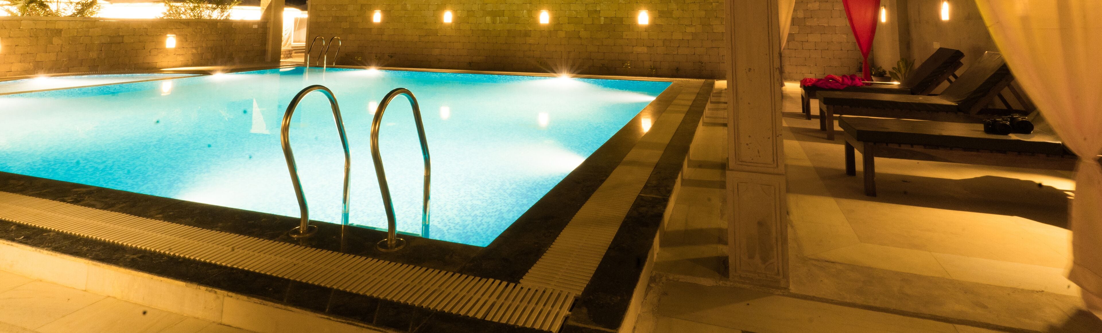 Una piscina interior rectangular con dos escaleras metálicas a un lado, rodeada de un solárium con baldosas.