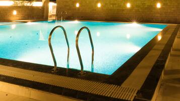 Una piscina interior rectangular con dos escaleras metálicas a un lado, rodeada de un solárium con baldosas.