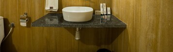 Un baño con lavamanos, dispensador de papel higiénico y artículos de tocador sobre la encimera.