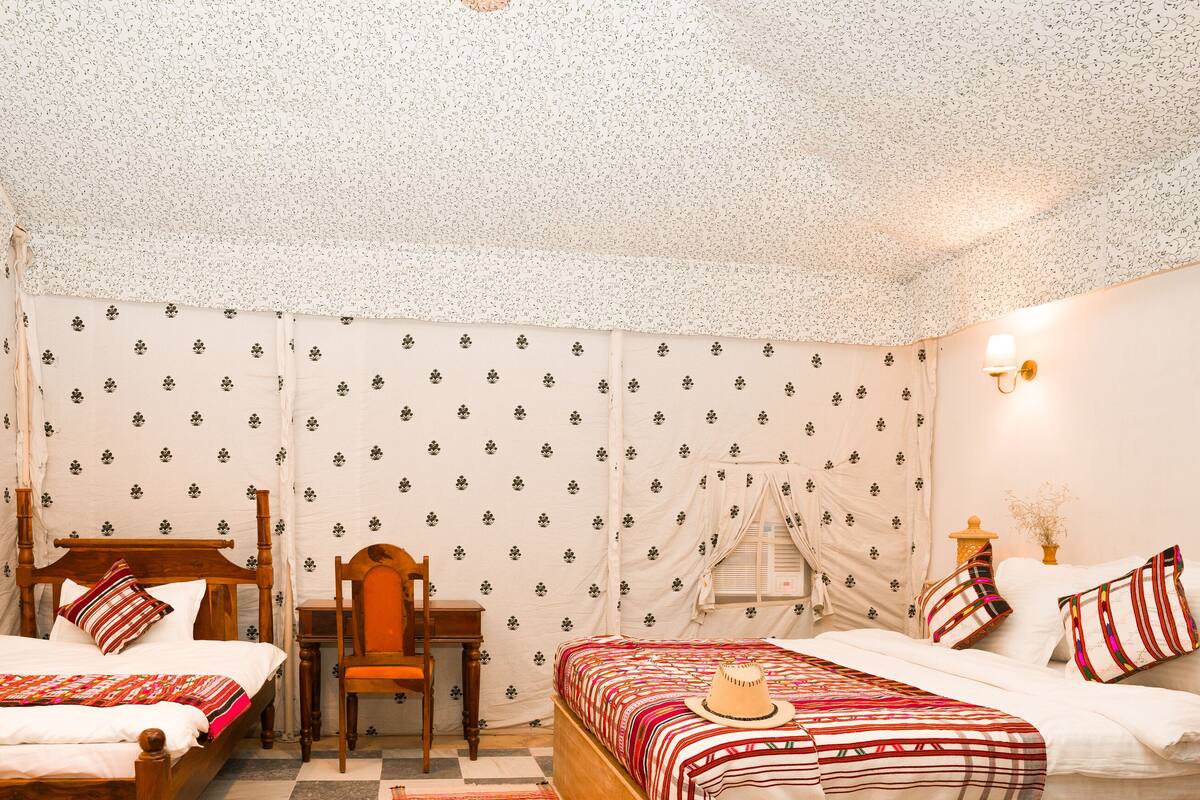 Een kamer met twee bedden, een houten stoel, een bureau en behang met een patroon.