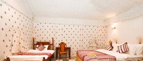 Una habitación con dos camas, una silla de madera, un escritorio y papel tapiz estampado.