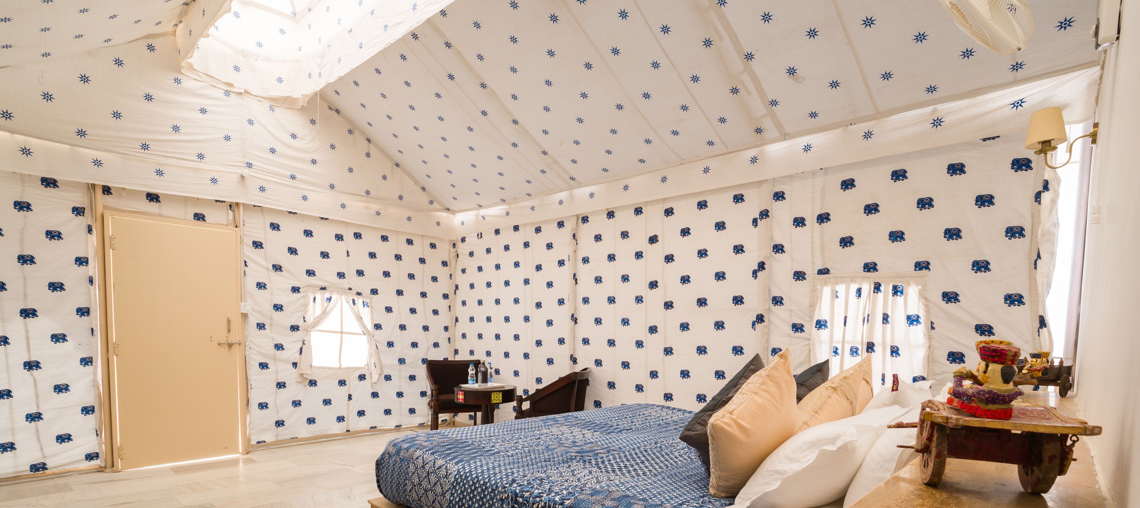 Een kamer met een gedessineerd plafond, een bed met een blauw-witte dekbedovertrek, een kleine tafel met een fles en een stoel.