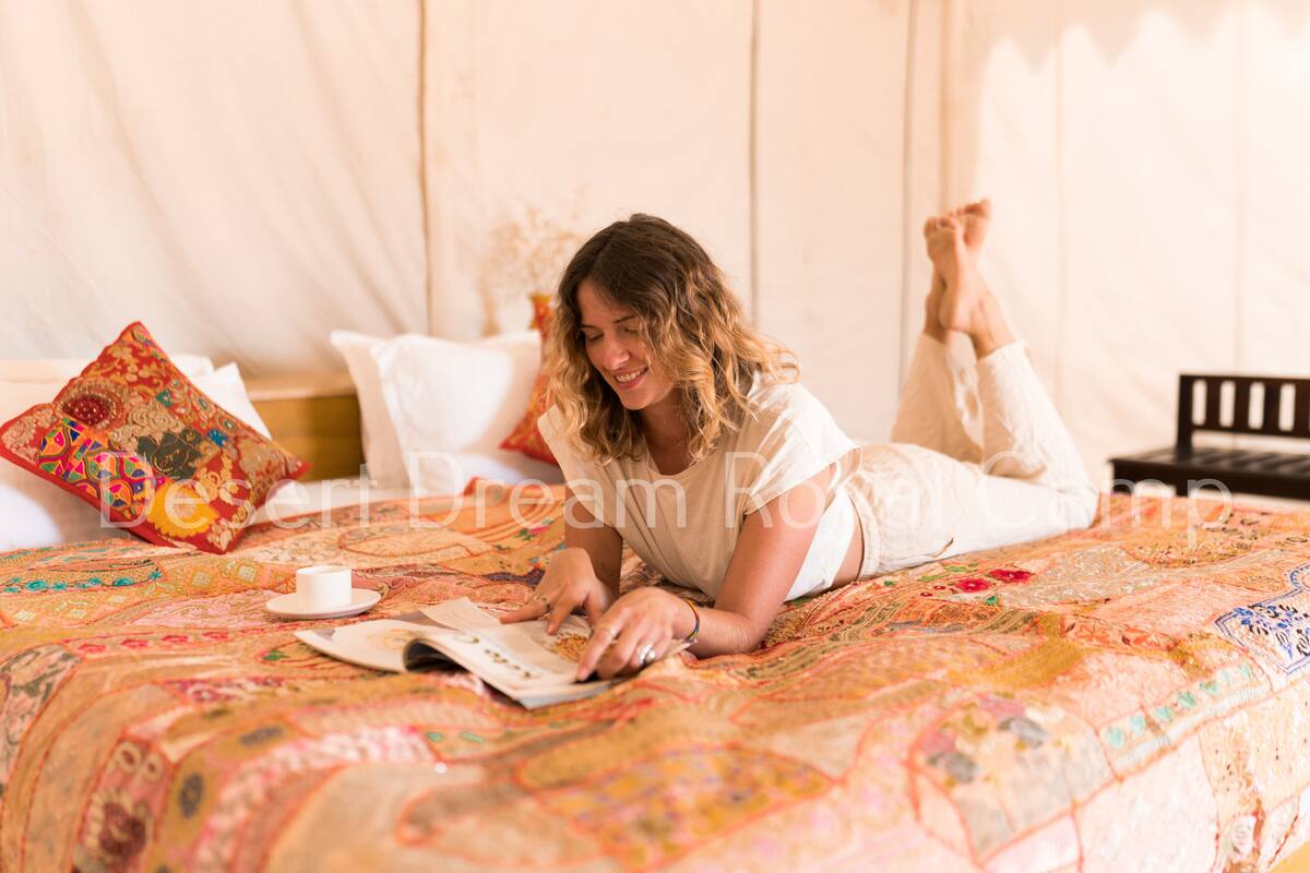 Iemand ligt op een bed met een kleurrijke quilt, een kopje en een boek.