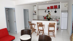 A modern kitchen with a central island, white cabinets, and a red countertop. There are wicker chairs and a red sofa in the adjacent living area. - Villa Maora (Koungou)