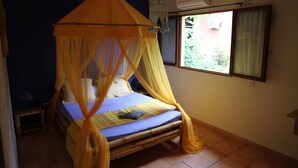 A bed with a canopy, a bedside table, a window with curtains, and an air conditioning unit. - Villa Maora (Koungou)