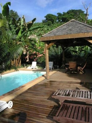 A wooden deck with a pool, surrounded by lush greenery and a gazebo. - Villa Maora (Koungou)
