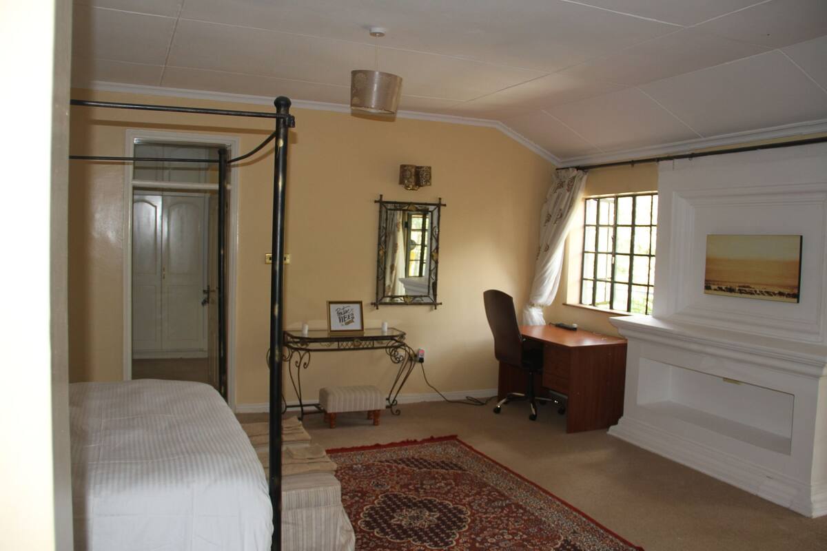 A bedroom with a bed, a desk, a chair, a window with curtains, and a fireplace.