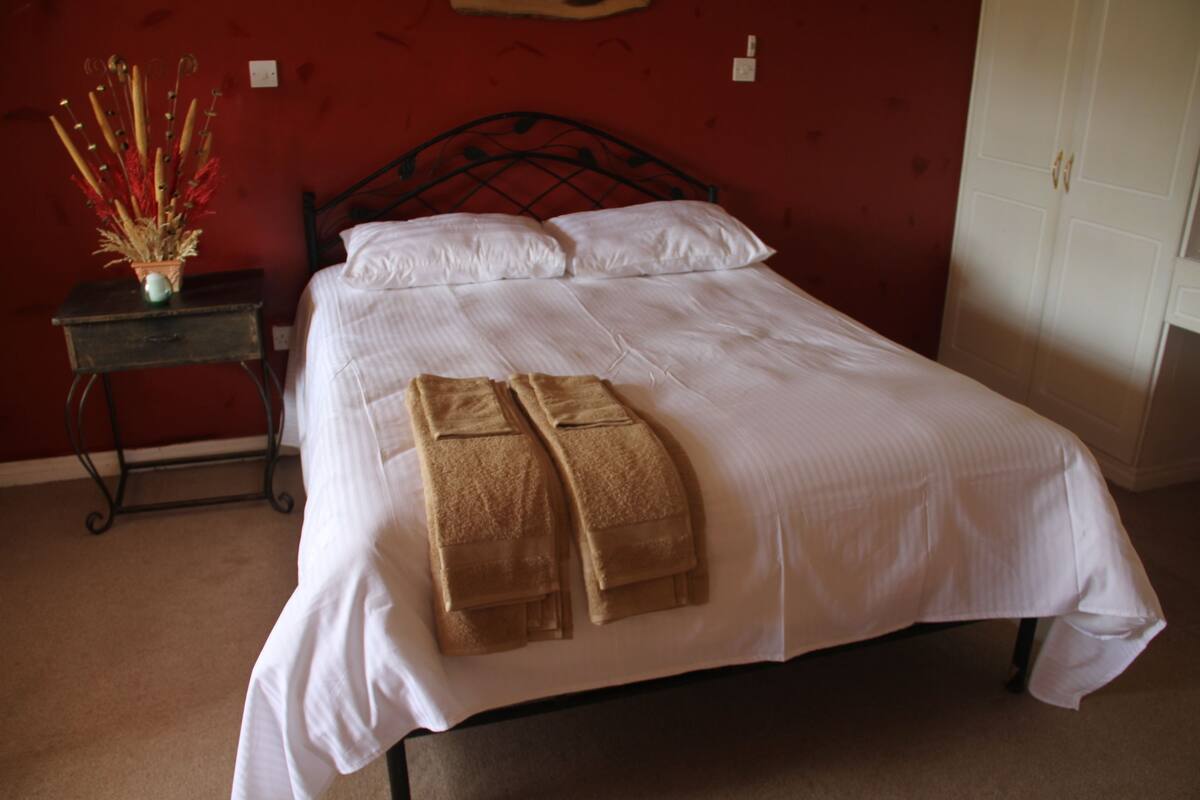 A neatly made bed with white linens and two brown towels placed at the foot.