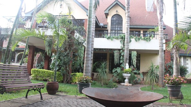 A courtyard with a bench, a large planter, and a house with a red roof and green accents. - Stunning Mansion (Nairobi)