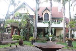 A courtyard with a bench, a large planter, and a house with a red roof and green accents. - Stunning Mansion (Nairobi)