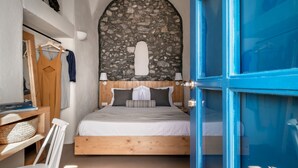 Un dormitorio con pared de piedra, cama de madera, puerta azul y una silla blanca.