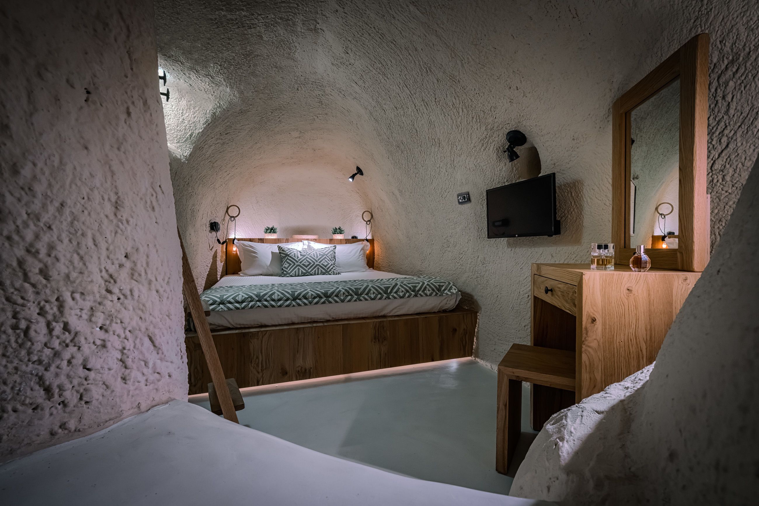 A cozy, rustic bedroom with a wooden bed, a small wooden desk, and a mirror.