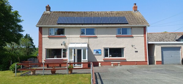 Un bâtiment à deux étages, doté de panneaux solaires sur le toit, d’une enseigne indiquant qu’il s’agit d’une maison d’hôtes et d’une cour avant clôturée.