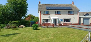 Ein zweistöckiges Haus mit einer Solaranlage auf dem Dach, einem eingezäunten Garten und einem kleinen Gemüsegarten.