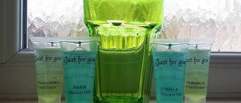 Estante de baño con botellas y tubos de vidrio verde etiquetados 'Just for you' que contienen champú, acondicionador y gel de ducha.